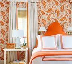 Bedroom with orange paisley wallpaper, white bedding, and orange accents.