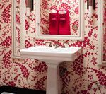 White pedestal sink with red floral wallpaper and a framed mirror.
