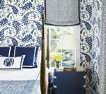 Blue and white bedroom with floral wallpaper, bed with pillows, and a window with a lamp and vase.