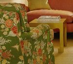 Green floral armchair next to a pink couch and yellow side table with books.