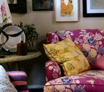 Close-up of a floral print sofa with yellow and pink pillows, next to a small side table and wall art.