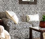 Black and white patterned sofa and wallpaper in a room, with white pillows and a potted plant.
