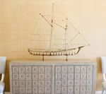 Metal ship sculpture on a decorative cabinet against a light yellow wall.