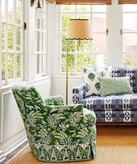 Green patterned armchair and blue patterned sofa in a sunroom with large windows and a floor lamp.