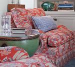 Floral patterned armchair and accent pillow beside a green ceramic side table. Books and objects are in the background.