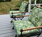 Two outdoor chairs with green floral cushions on a gray deck.