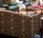 Couch with patterned brown fabric in living room with teal armchairs and red coffee table.