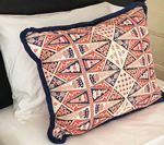 Decorative pillow with geometric pattern, dark blue trim, resting on white and black pillows.