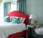 Red bed with turquoise accents in a bedroom, turquoise patterned wallpaper, and matching curtains.