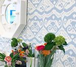 Flowers in vases against blue and white patterned wallpaper, near a white-framed mirror.