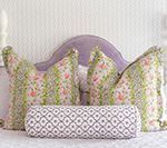 Bed with a lavender headboard and floral pillows, including a patterned bolster.