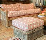 Wicker sofa and ottoman with pink and white checkered cushions, on a terracotta tile floor.