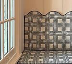 Built-in bench with a patterned back and seat, beside a white window.