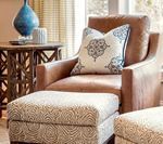 Brown leather armchair with patterned pillow and ottoman next to a wooden side table with blue decor.