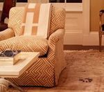 Upholstered armchair with geometric print and tan throw blanket, coffee table, and area rug.