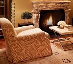 Cozy living room with patterned armchair facing a stone fireplace, small table with flowers.