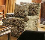 Upholstered armchair with geometric black and tan pattern; next to a table and curtains.
