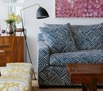 Living room with patterned sofa, wooden furniture, floor lamp, and artwork.