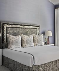 Bedroom with large bed, three pillows, ornate headboard, nightstand with lamp, and a window.