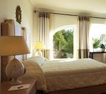 Bedroom with a double bed, lamp, and arched windows overlooking greenery.