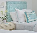 Bed with aqua patterned headboard, white pillows, and turquoise decorative pillow on white bedding.