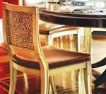 Wooden dining chair with patterned back, brown leather seat, and gold trim, near a round table.