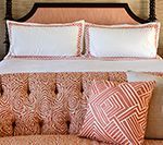 Bed with white sheets, coral trim, and patterned throw pillows.