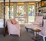 Bedroom with pink patterned chairs, ottoman, desk, and curtains; dark wood four-poster bed.