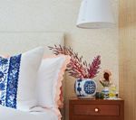 Bedroom with blue and white patterned pillow, pink flowers in a vase, and a nightstand.