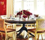 Elegant dining room with round table set for a meal. Red and gold decor.