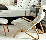 Chair with wooden frame and patterned fabric seat, next to a matching ottoman, in a bedroom setting.