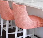 Two coral patterned bar stools at a white counter. White legs, black footrests.