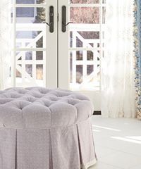 Tufted round ottoman with pleated skirt, in front of white French doors.