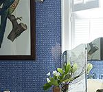 Blue patterned wallpaper with framed parrot print, flowers, and window.