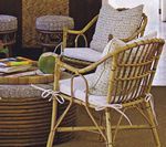 Rattan chairs with white cushions, a round ottoman, and a coconut on a table.