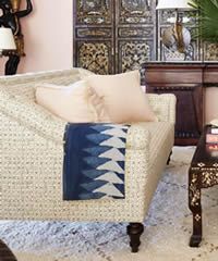 Beige sofa with blue patterned throw blanket in front of a decorative cabinet.