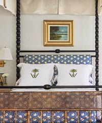 Bedroom with four-poster bed; headboard and bedding feature blue floral and white accent pillows; framed landscape art.