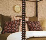 Bed with decorative pillows and a textured tan wallpaper background.