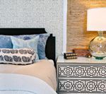 Bedroom with patterned nightstand, bed with blue pillows, and lamp.