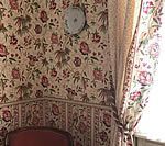 Floral patterned wallpaper and curtains in a room corner, with a ceiling light fixture.