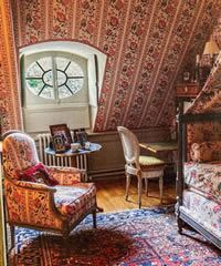 Cozy bedroom with floral wallpaper, window, armchair, and antique canopy bed.