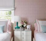 Twin beds in a pink-walled room with a shared white nightstand, teal lamp, and flower arrangement.