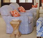A blue striped armchair with orange patterned pillows next to a wooden side table.