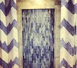 Shower with blue and white tile design, framed by curtains with zigzag pattern.