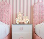 Pink and white striped wallpaper and a nightstand with a scooter light, flanked by pink upholstered headboards.