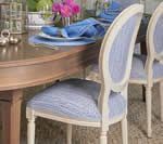 White dining chairs with blue patterned upholstery around a wooden table set for a meal.
