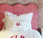 Pink scalloped headboard with white bedding and red polka dots and monogram.