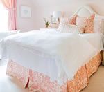 Pink and white bedroom with a patterned bed skirt, white bedding, and pink accents.
