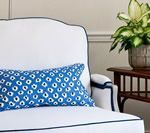 White armchair with blue patterned pillow, plant on a side table.