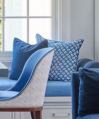 Blue upholstered chair with patterned pillow against a window seat with blue cushions.